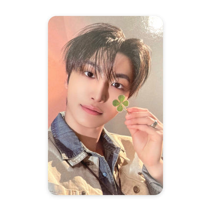 ATEEZ Seonghwa Blue Drift event photocard — dark swept hair, light denim shirt under a beige jacket, holding a four-leaf clover at his cheek with a silver ring, warm peach-pink background.