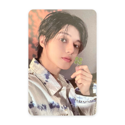 ATEEZ Wooyoung Blue Drift event photocard — long dark hair, blue-and-white tie-dye denim jacket, holding a four-leaf clover upright, red autumn leaves in the background.