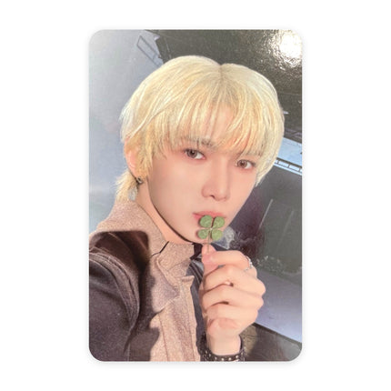 ATEEZ Yeosang Blue Drift event photocard — platinum-blond hair, brown jacket, holding a four-leaf clover to his lips, wristwatch visible, dark gray background.