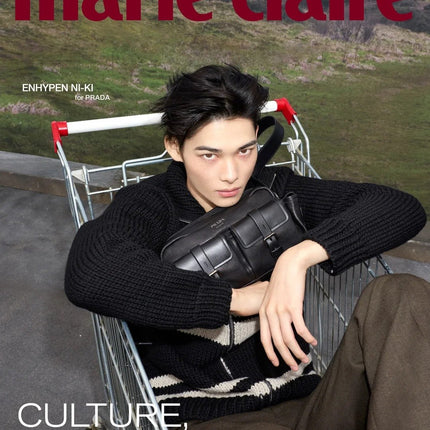 ENHYPEN Ni-ki Marie Claire Korea November 2026 Cover D, Ni-ki sitting in a shopping cart in a black chunky knit zip cardigan and olive trousers hugging a black leather Prada bag, grassy hillside behind, burgundy Marie Claire logo